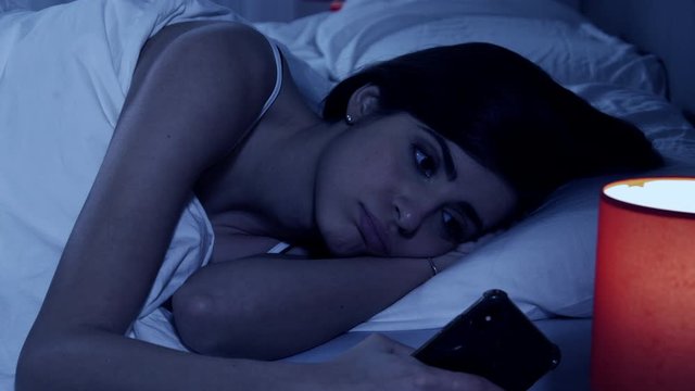 Woman suffering of insomnia looking cell phone at night closeup
