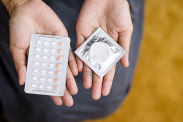 Woman hand holding contraceptive pills and condom sitting on sofa background,protection, safe sex,contraceptive means.