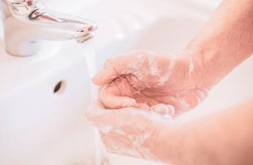 Close up of a man uses soap to wash his hands under the water tap - hygiene and prevention concept.