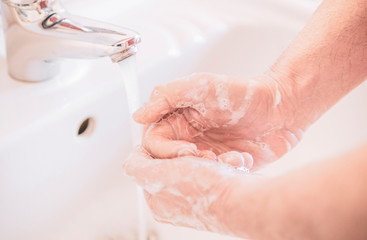 Fototapeta premium Close up of a man uses soap to wash his hands under the water tap - hygiene and prevention concept.