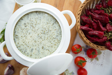 Dovga in the on wooden board . National food of azerbaijan . Creamy soup dovga . Azerbaijani Dovga soup with greens on a white bowl . Red tomato . Red Dry Pepper in Traditional Basket .