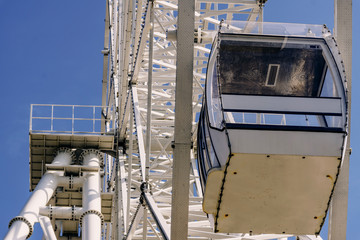White metal construction of an attraction Ferris wheel with a viewing cabin against a blue sky