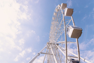 White metal construction of an attraction Ferris wheel with observation cabs high against a blue sky with white clouds.
