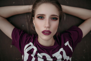 Portrait of a young girl holding her hair with her hands behind her head in a T-shirt and bright makeup