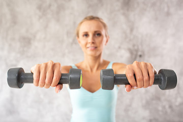 Blond woman in blue top holds two dumbbells in her hands. Selective focus