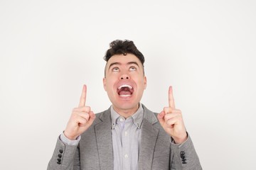 Charming carefree man with positive expression, points up with both index fingers, dressed in...