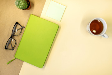 composition black glasses, notebook for notes, cactus, cup with tea on a yellow background. Flat lay and top view photo.