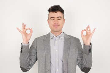 Meditation, religion and spiritual practices. Handsome young blond haired male doing yoga in the morning indoors after waking up, keeping eyes closed, holding fingers in mudra gesture.