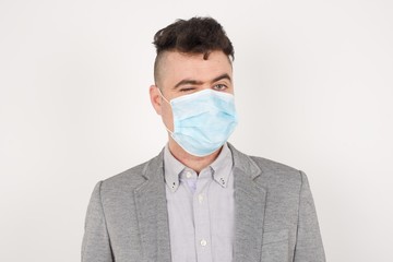 Cute young blond male wearing medical mask blinking his eyes with pleasure having happy expression. Facial expressions and people emotions concept.