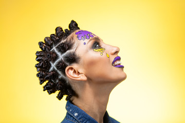 profile of a girl on a yellow background with an original creative afro hairstyle in the form of horns, with colored blots on the face with lenses and violet lips