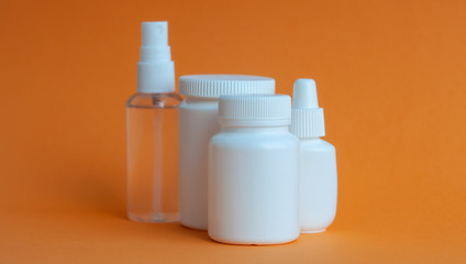Close-up of three portable plastic bottles with tablets and vitamins and one transparent plastic bottle with a disinfectant antiseptic gel on the table. Orange textured background.