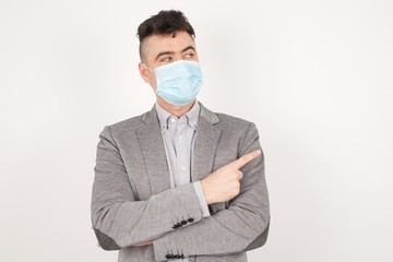 Portrait of young man wearing medical mask posing on camera with tricky look and gesturing to side. Male designer presenting lovely product with index finger. Gesture concept.