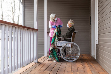 Woman and man in wheelchair wearing protective mask to prevent coronavirus transmission on porch