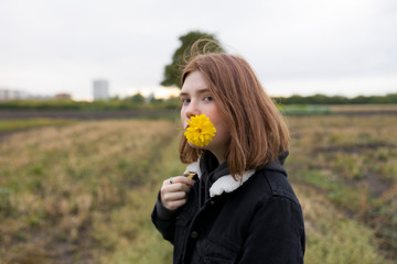 Teenage girl holding yellow flower in field