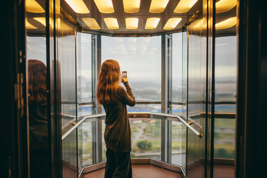 Young woman taking picture while standing in transparent elevator