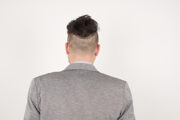 The back view of a guy wearing casual clothes standing against gray wall. Studio Shoot.