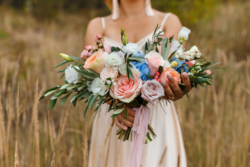 A delicate and very beautiful wedding bouquet of roses, greenery, eustoma and hydrangea in brides hands. Bridal trendy florists in pastel colors. Handle decorated with pink ribbons