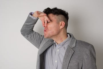 young man with disgust on his face pinches nose, something stinks, very bad smell isolated on gray background. Negative emotion facial expression