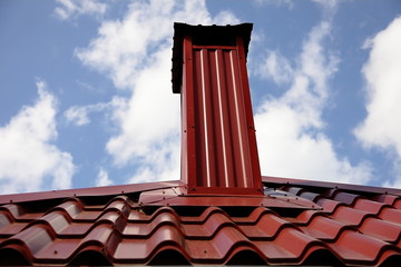 Chimney. Chimney on the roof of a house made of red-brown metal tile with a fungus on top.