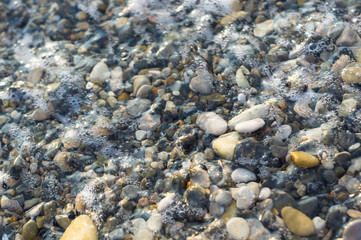 pebble stones on the sea beach, the rolling waves of the sea with foam
