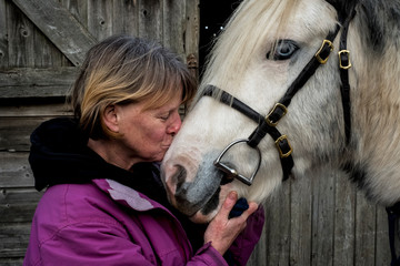 Close up of mature woman kissing cob horse outside stable