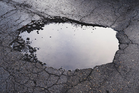 Water filled pothole on urban street with cracks and fracture marks