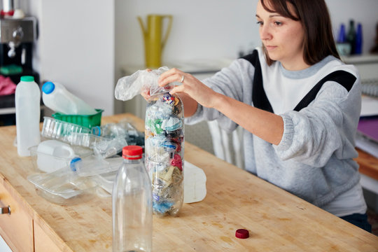 Woman stuffing soft waste plastics into large plastic bottle to make an ecobrick for use as a  building block