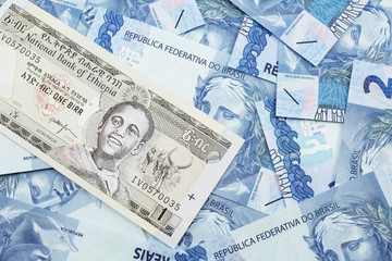 A close up image of a one Ethiopian birr bank note on a background of Brazilian two reais bank notes