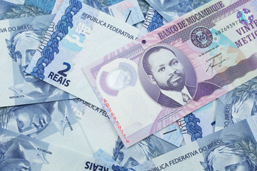 A close up image of a purple, twenty metical bank note from Mozambique on a background of Brazilian two reais bank notes