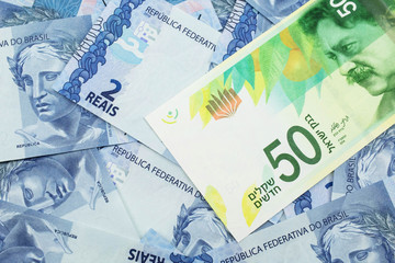 A close up image of a fifty shekel bank note from Israel on a background of Brazilian two reais bank notes in macro