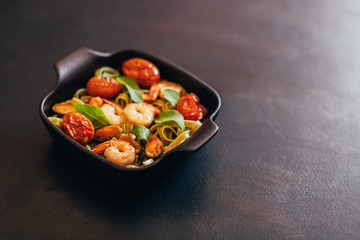 fettuccine with shrimp in a black bowl on a black background.