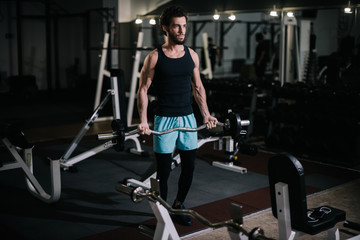 Fototapeta na wymiar Sportive bearded young man with muscular wiry body wearing sportswear holding barbell during sport workout training in modern dark gym. Concept of healthy lifestyle.