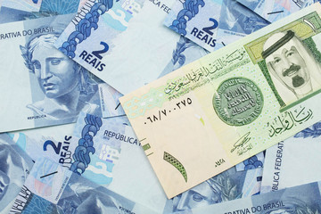 A close up image of a one riyal bank note from Saudi Arabia on a background of Brazilian two reais bank notes in macro
