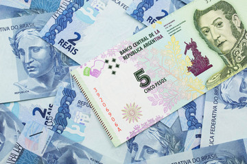 A five peso bank note from Argentina on a background of Brazilian two reais bank notes close up