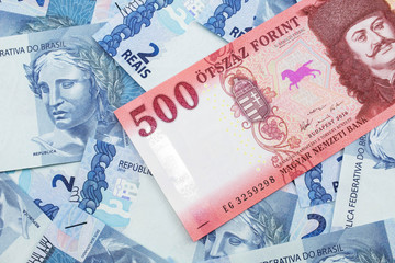 A close up image of a red Hungarian five hundred forint bank note with Brazilian two reais bank notes in the background