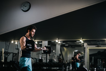 Fototapeta na wymiar Slim bearded young man with muscular wiry body wearing sportswear lifting barbell during sport workout training in modern dark gym. Concept of healthy lifestyle.