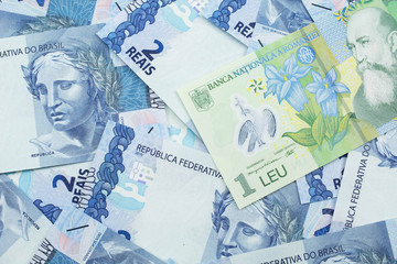 A close up image of a green Romanian one leu bank note on a background of Brazilian two reais bank notes