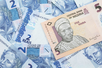 Fototapeta premium A close up image of a peach colored, five Nigerian naira bank note on a background of Brazilian two reais bank notes