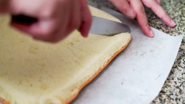 Indian girl cutting the edges of a flat thin sheet of cake to trim the edges and make them straight and perfect for a beautiful cake