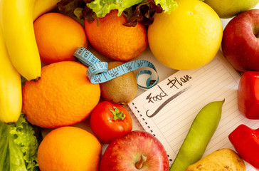 Diet plan notebook and vegetables for healthy food concept. Various fruits and vegetables and measuring tape.