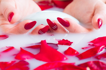 Close up female hands hold soap against the background of milk or white water with rose petals