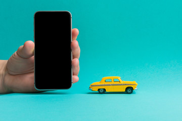 Taxi mobile online application concept.  Hand holding smart phone.Toy yellow taxi car model.