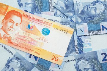 An orange twenty piso bank note from the Philippines with Brazilian two reais bank notes close up...