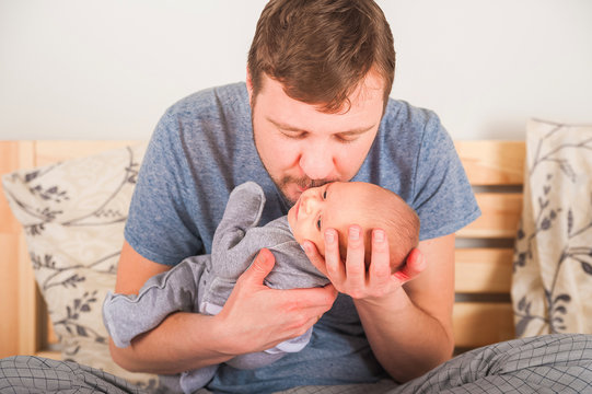 Father And Newborn In Scandi Bedroom Interior. The Father Sings A Lullaby To The Child. Parent Calms The Baby Before Going To Bed In His Arms. Home Care And Baby Care Concept.