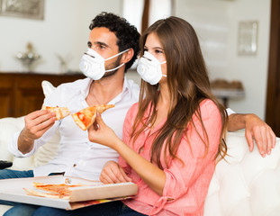 Couple eating pizza at home while wearing a mask