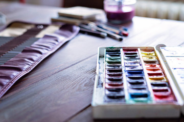 color pencils, brushes and watercolor paints on wooden table. art painter accessories , selective focus.