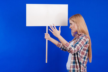 Emotional young blonde woman with a white banner for slogans in her hands expresses a protest and...