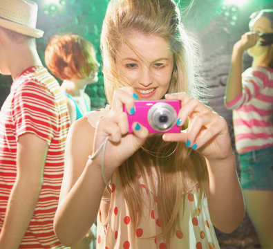 Playful teenage girl using digital camera at party
