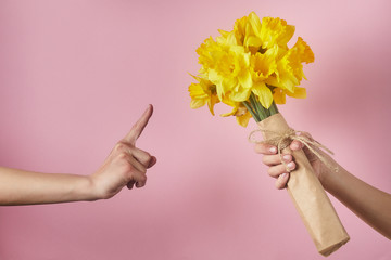 Man's hand gives bouquet of yellow narcissus flowers to girl and receives refusal, woman shows Attention sign