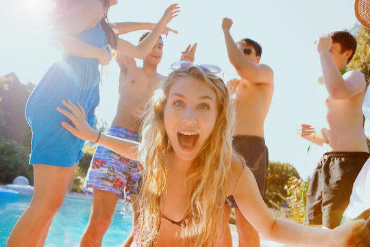 Portrait exuberant teenage girl dancing with friends at sunny summer poolside